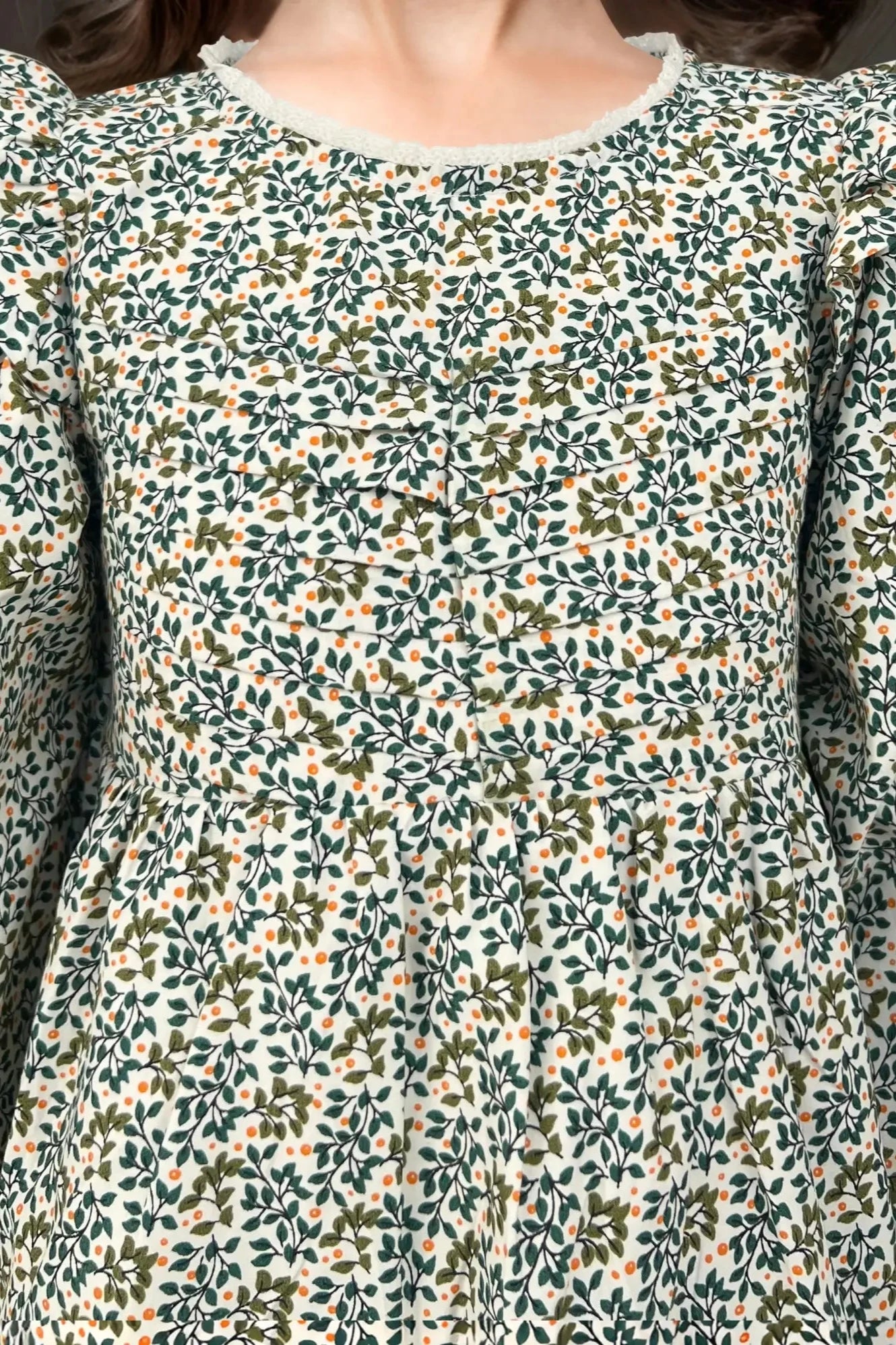Close up view of a green dress for baby girl, designed for kids aged 2 to 9 years old.