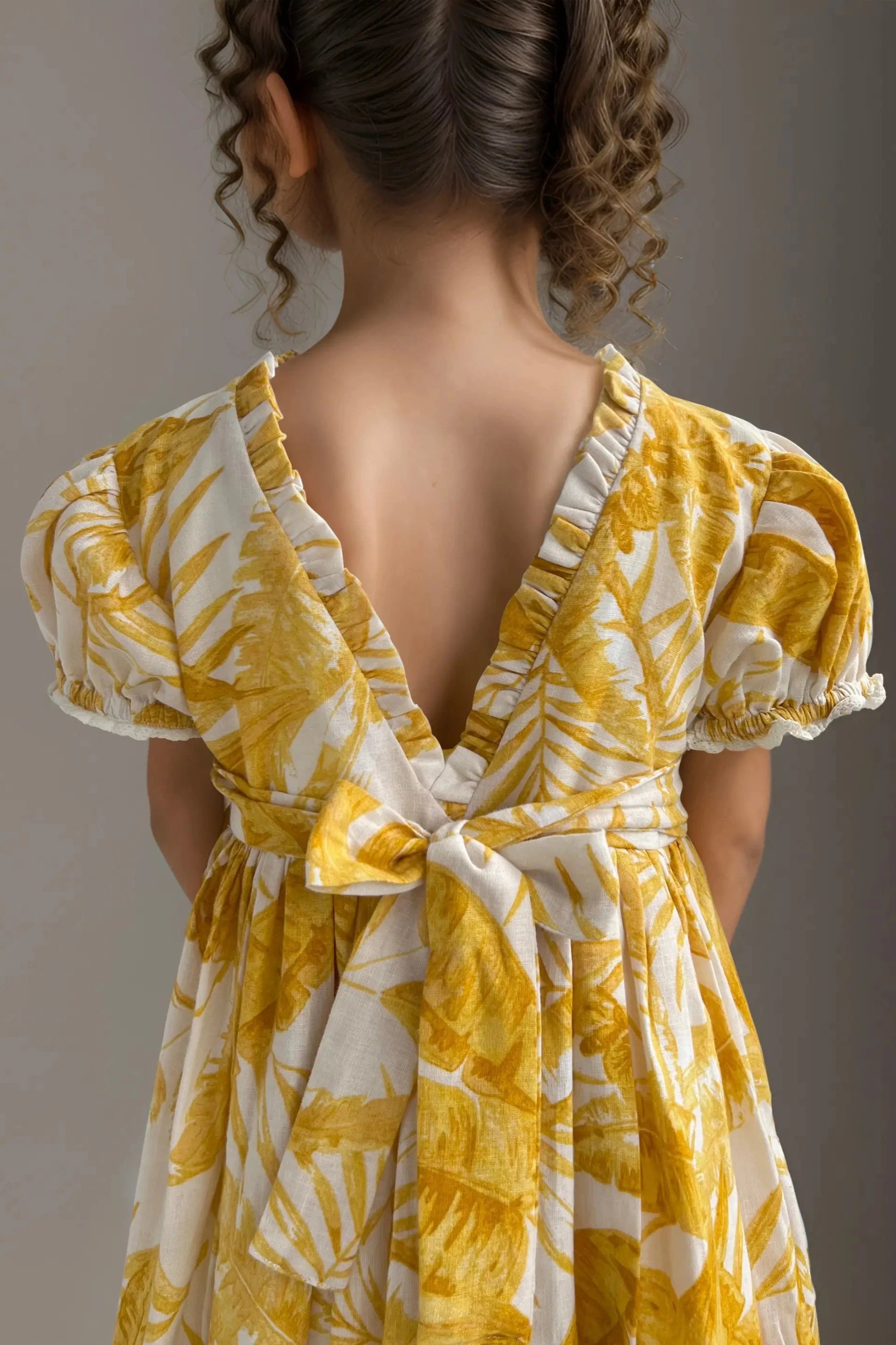 Full back close up view of a yellow floral printed balloon dress for girls, made of cotton.