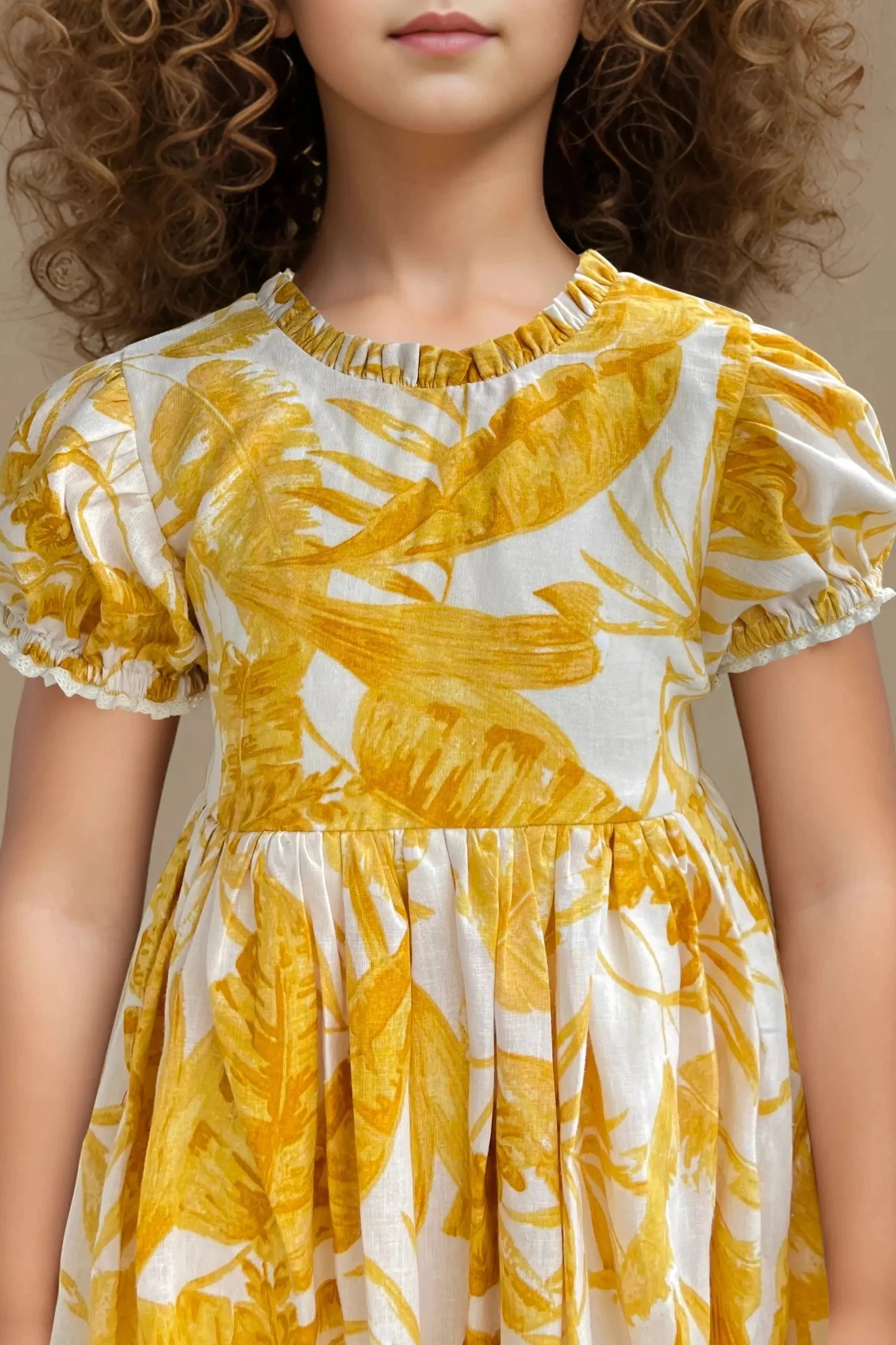 Full front close up view of a yellow floral printed balloon dress for girls, made of cotton.